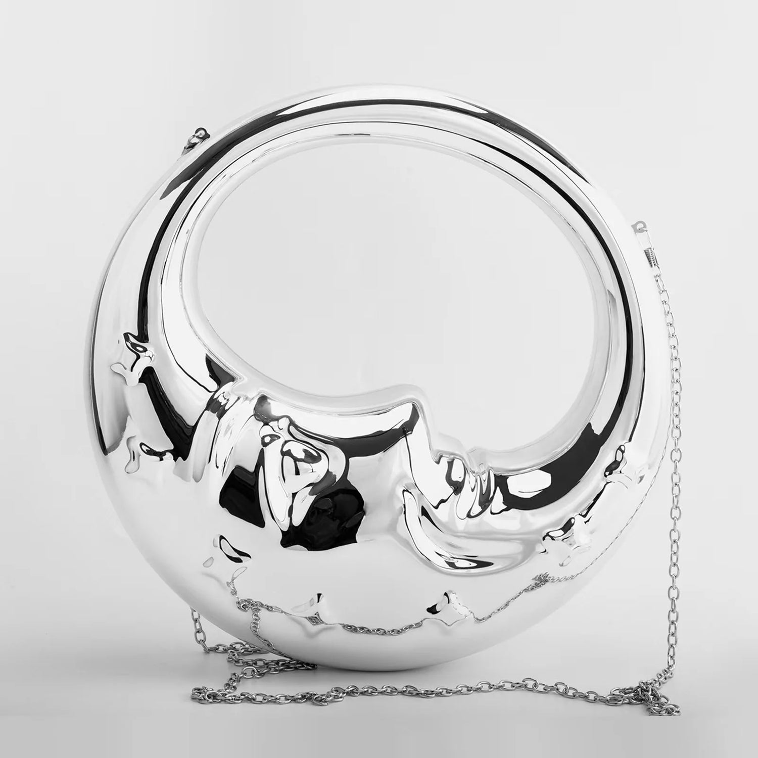 A silver crescent moon-shaped clutch bag with a glossy acrylic finish, featuring carved stars and a whimsical face etched into the moon. It has a detachable shoulder strap.