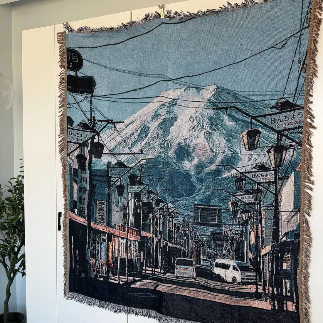 Woven blanket with a scenic design of a mountain and street scene, displayed on a white surface.