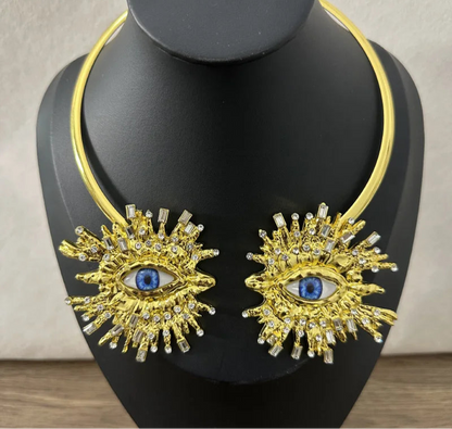 Gold necklace with eye design on a black mannequin against a neutral background